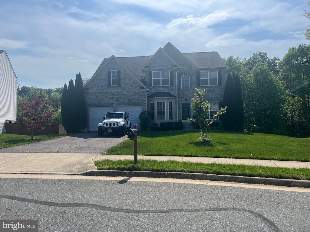 view of front of house with an attached garage, a front lawn, stone siding, and aphalt driveway