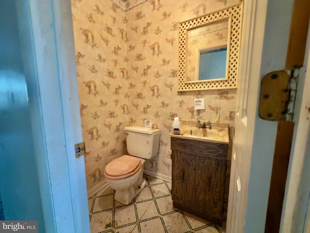 bathroom with toilet, wallpapered walls, baseboards, and vanity