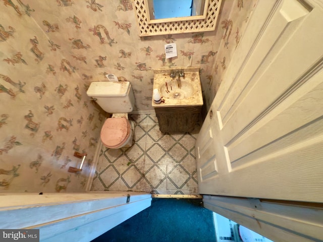 half bathroom with a sink, toilet, and wallpapered walls