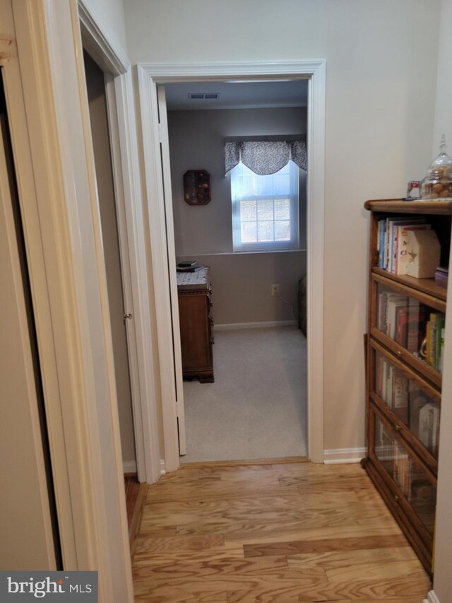 hallway with baseboards, light wood finished floors, and visible vents