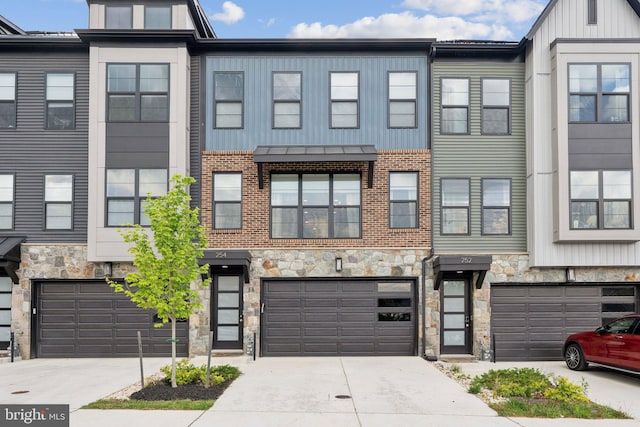 townhome / multi-family property with board and batten siding, an attached garage, driveway, and stone siding