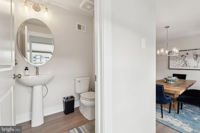 half bathroom with a chandelier, toilet, wood finished floors, and visible vents