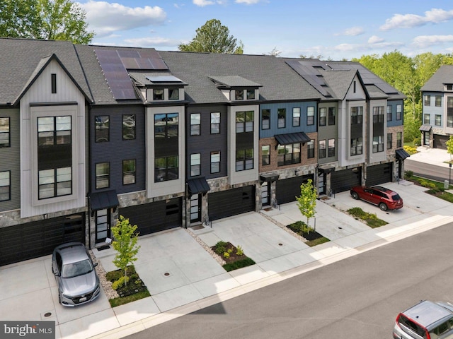 multi unit property featuring solar panels, a residential view, a garage, concrete driveway, and stone siding