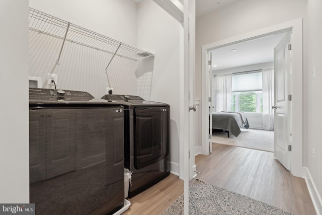 clothes washing area with washer and dryer, laundry area, baseboards, and light wood-style flooring