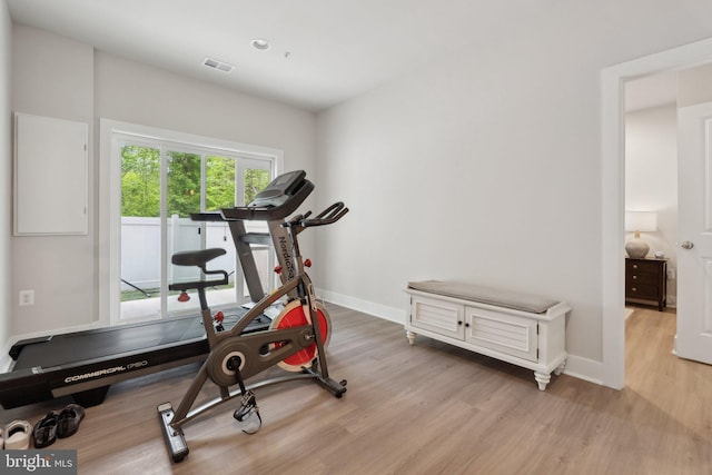 exercise area with visible vents, light wood finished floors, and baseboards