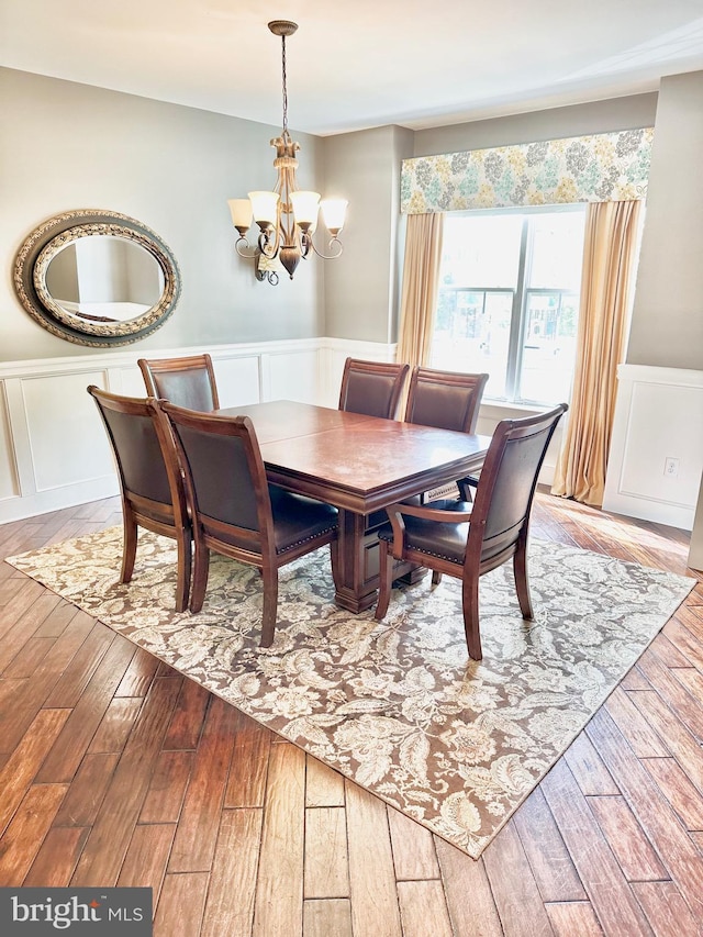 dining space with a decorative wall, an inviting chandelier, light wood finished floors, and a wainscoted wall