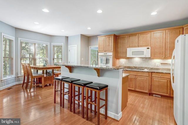 5985 Twin Branch Ct, Haymarket, VA 20169 - kitchen with tasteful backsplash, light stone countertops, light wood-style floors, a breakfast bar, and white appliances