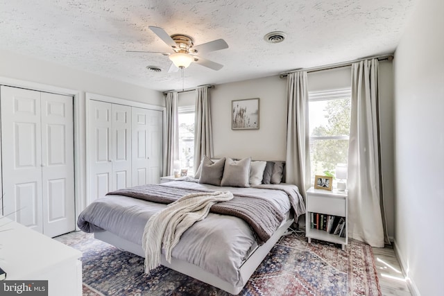 bedroom with two closets, a textured ceiling, visible vents, and ceiling fan