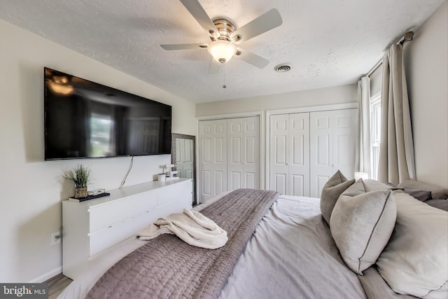 bedroom with a ceiling fan, a textured ceiling, visible vents, baseboards, and multiple closets