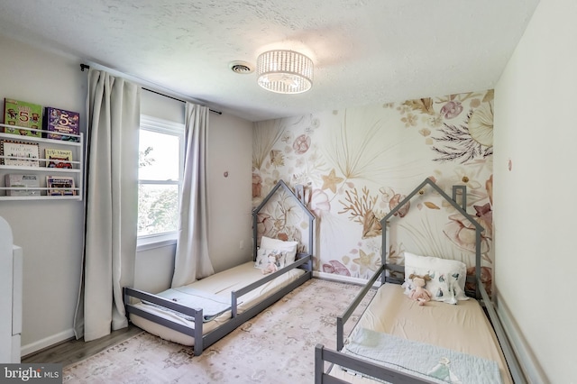 bedroom featuring a textured ceiling, a chandelier, wallpapered walls, wood finished floors, and visible vents
