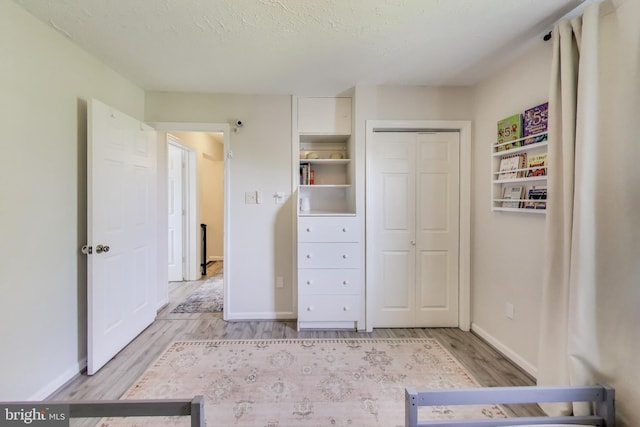 unfurnished bedroom featuring a textured ceiling, baseboards, light wood finished floors, and a closet