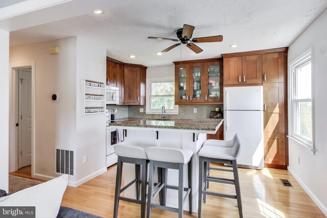 kitchen with decorative backsplash, a kitchen breakfast bar, white appliances, and visible vents