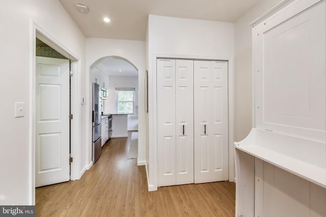 corridor with light wood-type flooring, arched walkways, and recessed lighting