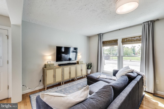 living room featuring visible vents, a textured ceiling, baseboards, and light wood-type flooring
