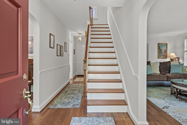 stairway featuring arched walkways, baseboards, and wood finished floors