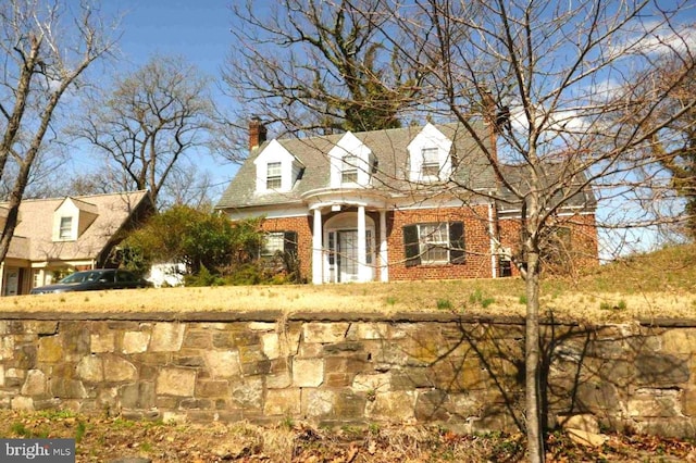 cape cod house with brick siding and a chimney
