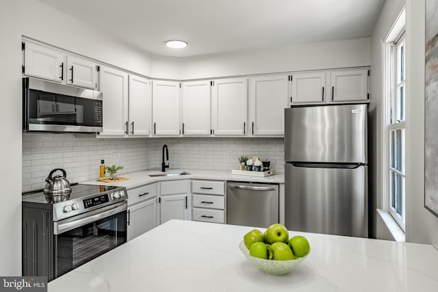 kitchen with decorative backsplash, appliances with stainless steel finishes, a sink, light stone counters, and white cabinetry