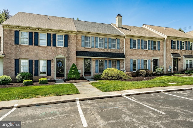 view of property featuring brick siding, a front lawn, uncovered parking, and a chimney