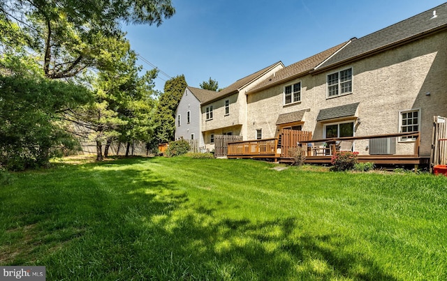 rear view of house featuring a lawn, stucco siding, and a deck
