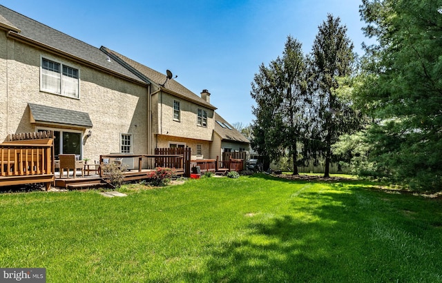 rear view of property with a lawn, a deck, a chimney, and roof with shingles