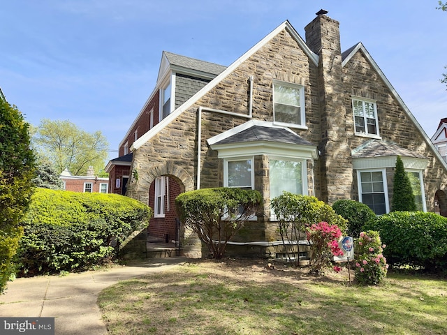 tudor-style house featuring a chimney and stone siding