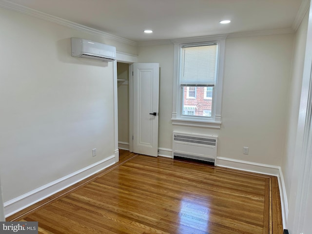unfurnished room featuring a wall mounted air conditioner, radiator heating unit, baseboards, wood finished floors, and ornamental molding