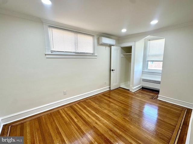 unfurnished bedroom featuring crown molding, baseboards, a wall unit AC, and wood finished floors