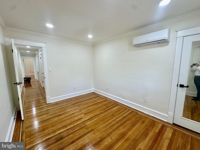 unfurnished room featuring baseboards, a wall unit AC, wood finished floors, and ornamental molding