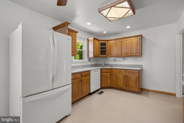 kitchen featuring brown cabinetry, a skylight, light countertops, recessed lighting, and white appliances