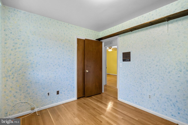 empty room featuring baseboards, wallpapered walls, and light wood-type flooring