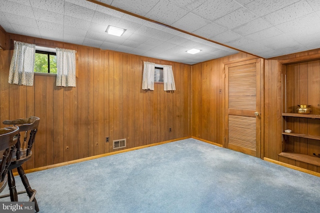 below grade area with carpet floors, wood walls, and visible vents