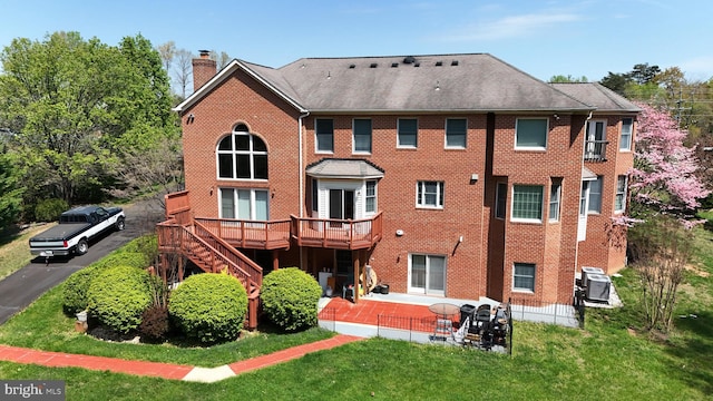 rear view of property with brick siding, a wooden deck, a chimney, a patio, and a yard