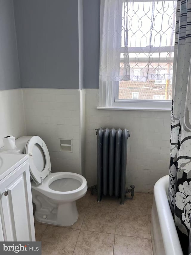 bathroom with tile walls, wainscoting, tile patterned floors, toilet, and radiator