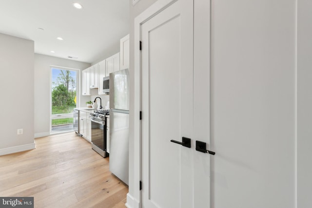 kitchen with baseboards, recessed lighting, white cabinets, light wood finished floors, and appliances with stainless steel finishes