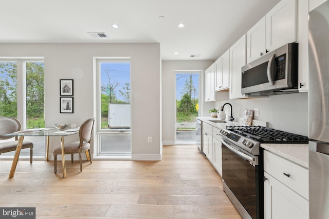 kitchen featuring baseboards, light wood-type flooring, white cabinets, a sink, and appliances with stainless steel finishes