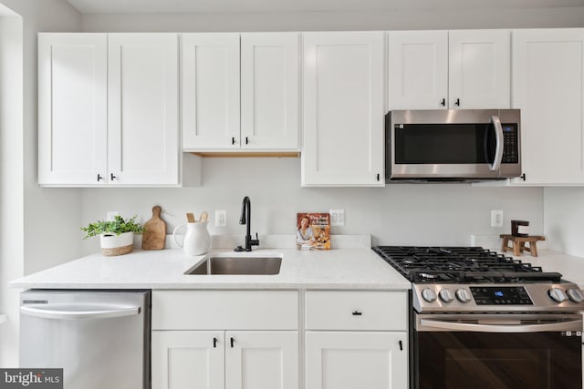 kitchen with white cabinets, stainless steel appliances, light stone counters, and a sink