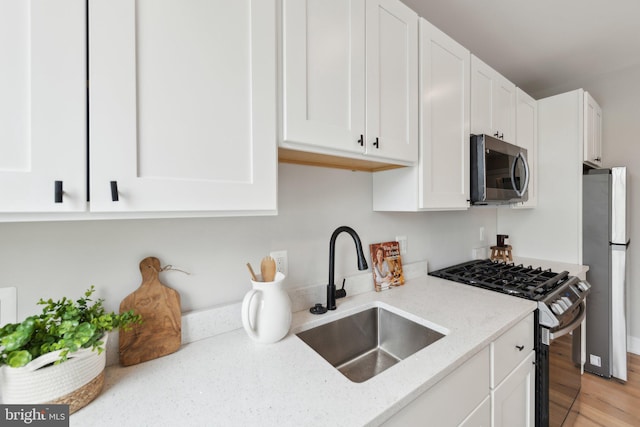 kitchen featuring white cabinets, light stone countertops, a sink, stainless steel appliances, and light wood-type flooring