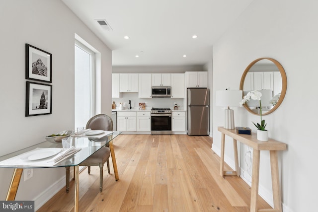 kitchen with a sink, stainless steel appliances, white cabinetry, light wood-type flooring, and visible vents