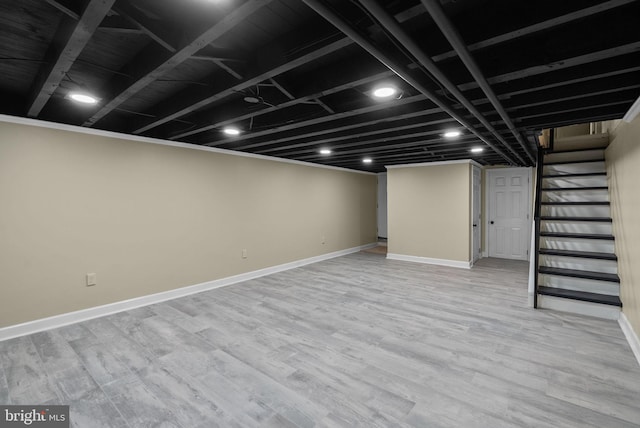finished below grade area with baseboards, light wood-type flooring, and stairs