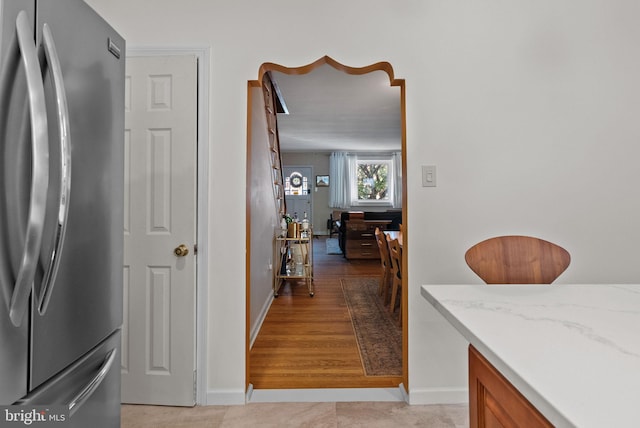 interior space featuring baseboards, freestanding refrigerator, brown cabinetry, and light stone countertops