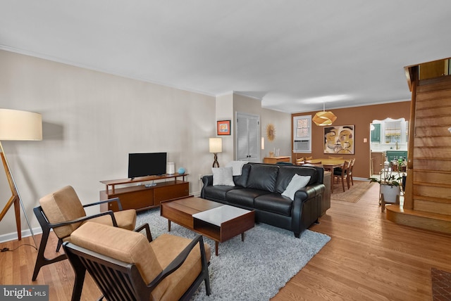 living area with cooling unit, light wood-style flooring, baseboards, ornamental molding, and stairway