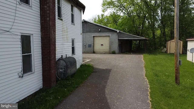 view of side of property with heating fuel, an outbuilding, a garage, a storage shed, and asphalt driveway