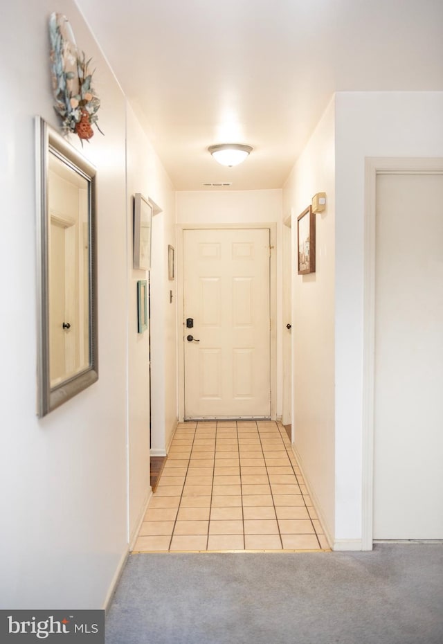 hall with baseboards, light tile patterned floors, and light colored carpet