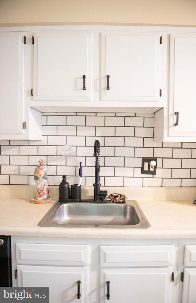 kitchen with a sink, tasteful backsplash, white cabinets, and light countertops