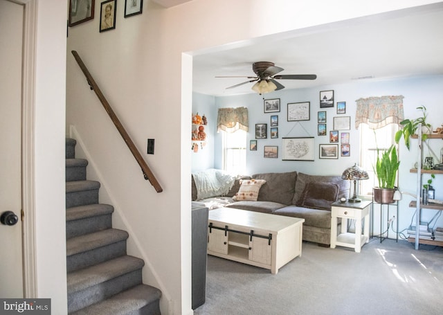 living room featuring a ceiling fan, light colored carpet, and stairway