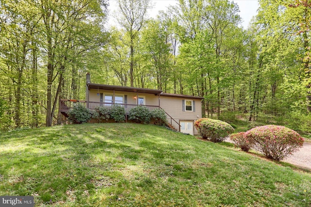 view of front of home featuring a wooden deck, a chimney, stairway, and a front yard