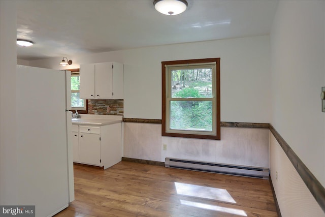 kitchen with freestanding refrigerator, wainscoting, baseboard heating, light wood-type flooring, and white cabinetry
