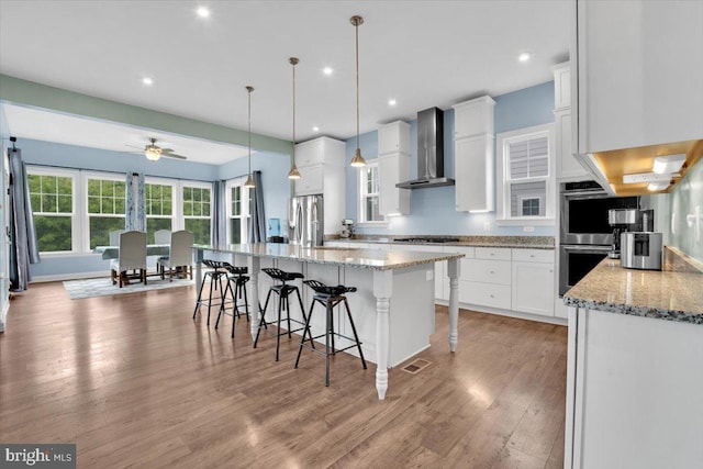 40918 White Clover Ln, Aldie, VA 20105 - kitchen featuring wall chimney exhaust hood, stainless steel appliances, light wood-style floors, a breakfast bar area, and white cabinets