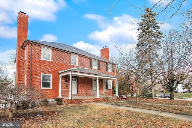 traditional home with a porch, brick siding, a chimney, and a shingled roof