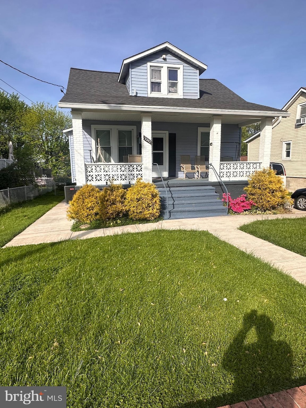 bungalow with a porch, roof with shingles, fence, and a front yard